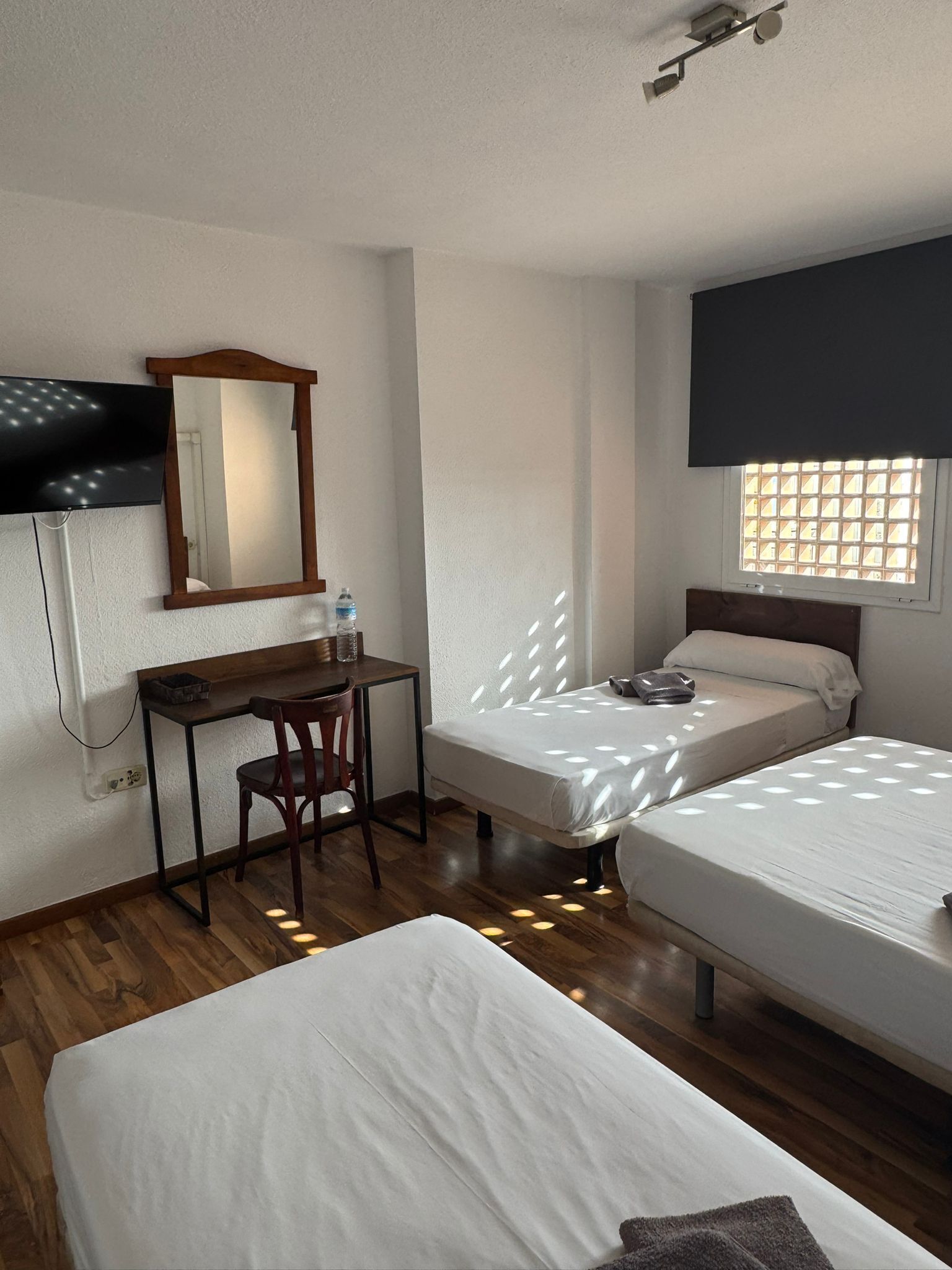 Ein Hotelzimmer mit zwei Einzelbetten, einem Schreibtisch mit Stuhl, einem Spiegel, einem Fernseher und einem Fenster mit Blick.