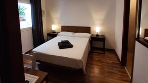Ein Hotelzimmer mit einem Bett, zwei Nachttischen mit Lampen, Holzboden und einem Vorhangfenster.