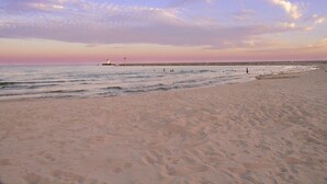 A beach with a lighthouse in the distance, sandy shore, and calm sea.