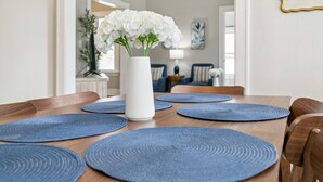 A dining table with blue placemats and a white vase with white flowers.