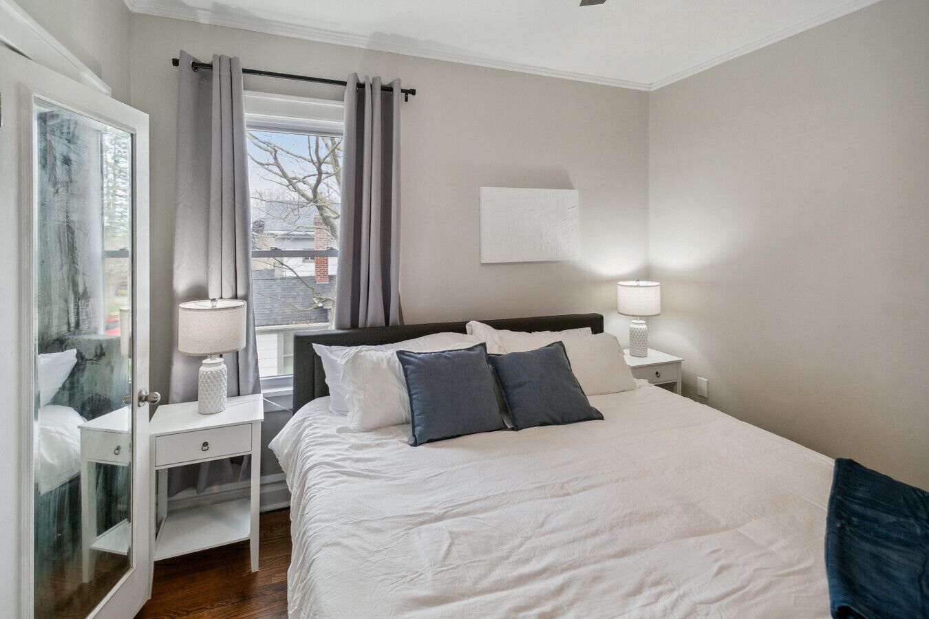 Un dormitorio con cama, mesitas de noche, un espejo y una ventana con cortinas.