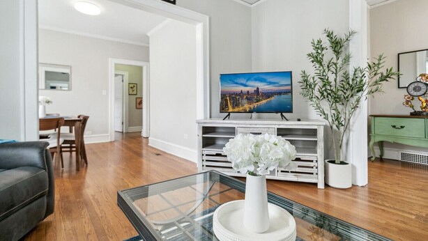 A modern living room with a flat-screen TV, a glass coffee table with a white vase, and a green cabinet.