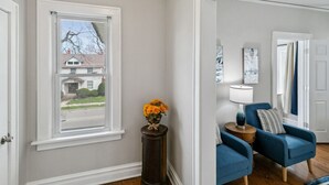 A room with a window, a blue armchair, a lamp, and a vase with flowers.