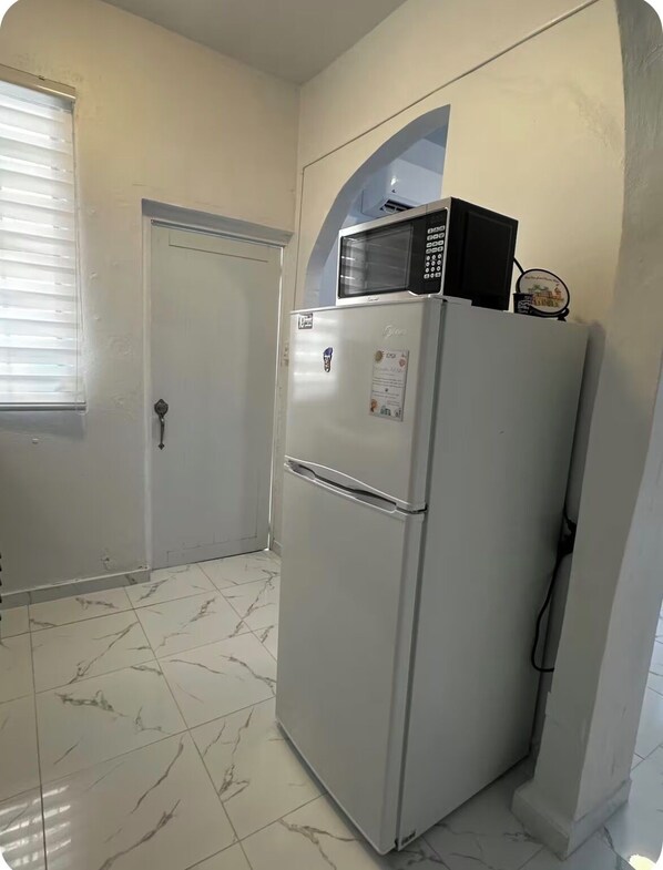 A compact kitchen with a refrigerator, microwave, and a door with a handle.