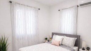 Ein Schlafzimmer mit Bett, Vorhängen, Nachttisch, Lampe und einer Zimmerpflanze.