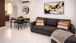 Ein modernes Wohnzimmer mit einem grauen Sofa, zwei gemusterten Zierkissen, einem runden Spiegel und einem gerahmten abstrakten Gemälde.