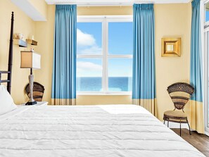 Ein Schlafzimmer mit einem großen Bett, einem Fenster mit Meerblick und zwei Korbstühlen.