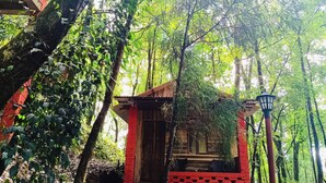 A small wooden structure with a red exterior, surrounded by dense green foliage. - Orion Retreat (Darjeeling)