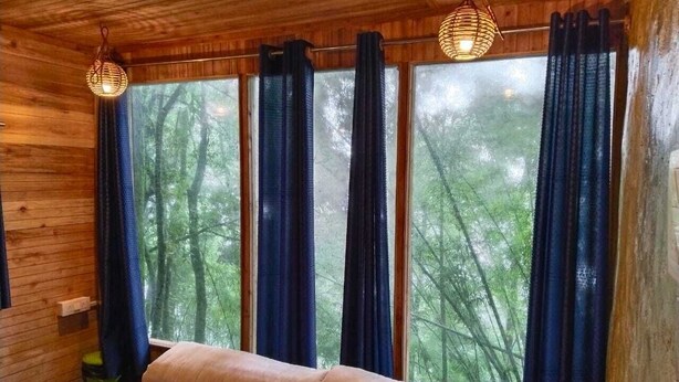A room with a wooden interior, a large window with curtains, a patterned rug, and a wooden bench. - Orion Retreat (Darjeeling)
