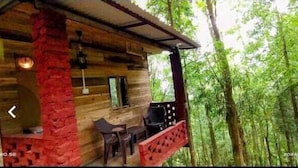 A wooden cabin with a porch, a stone wall, and a view of dense forest. - Orion Retreat (Darjeeling)