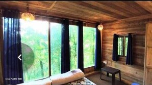 A wooden cabin room with large windows, a bed, a small table, and a mirror. - Orion Retreat (Darjeeling)