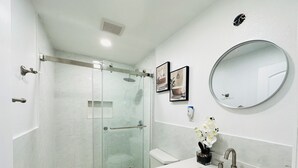 Et moderne badeværelse med bruseniche i glas, toilet, vask med spejl og dekorative elementer.