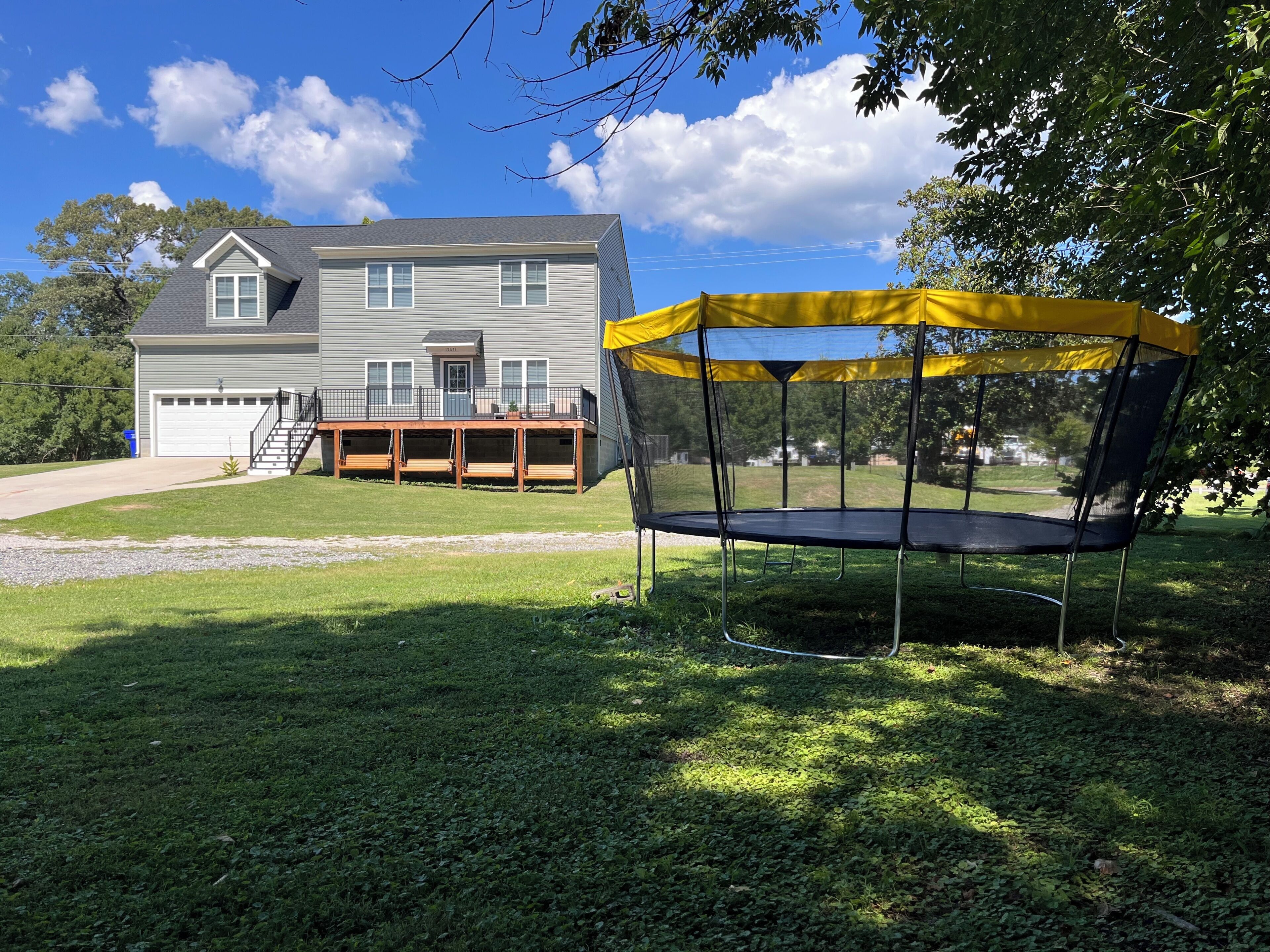Une maison d’habitation avec une terrasse à l’avant et un trampoline doté d’un filet de sécurité jaune.