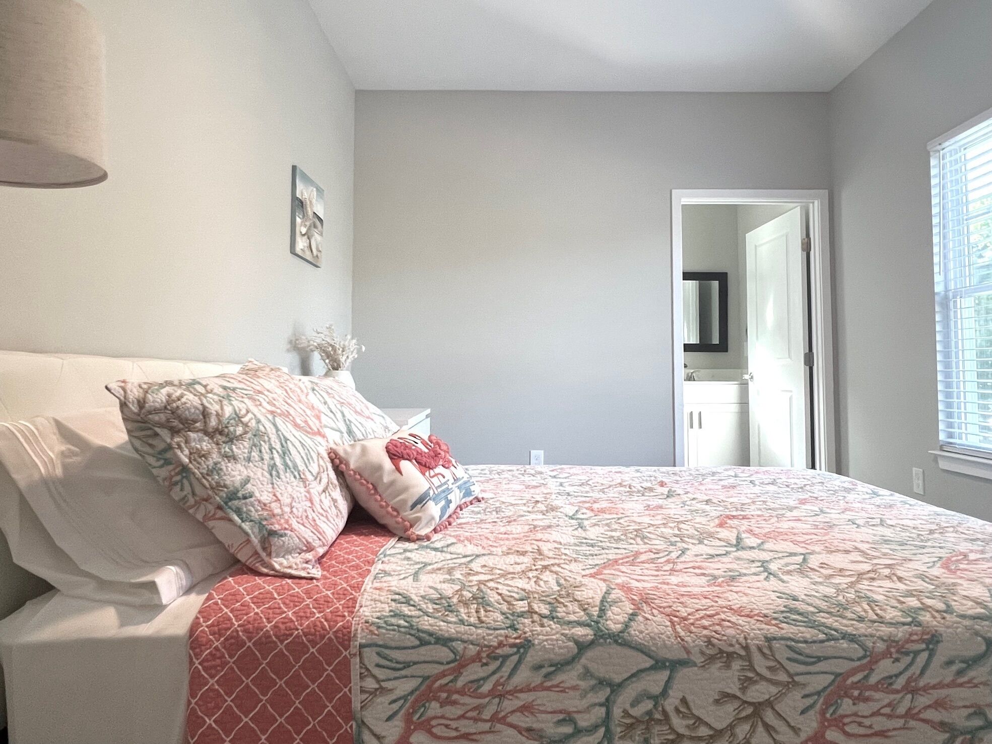 A bedroom with a bed, pillows, a bedside table, a lamp, and a door leading to another room.