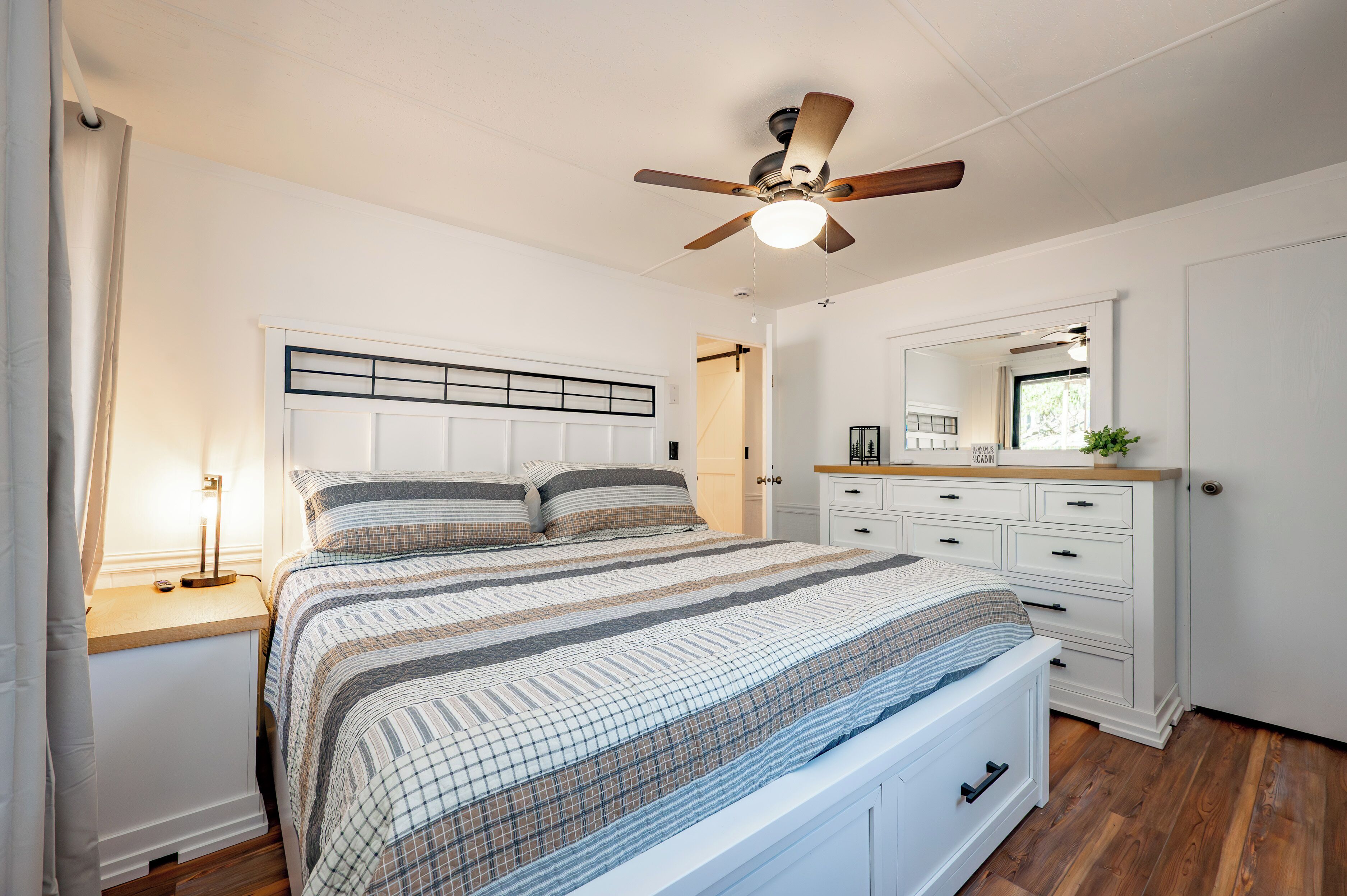Un dormitorio con cama, mesitas de noche, cómoda, ventilador de techo y espejo.