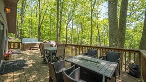 Una terraza de madera con mobiliario exterior, un jacuzzi y vistas a un bosque.