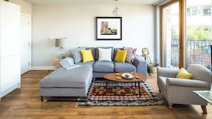 Ein modernes Wohnzimmer mit einem grauen Ecksofa, einem gemusterten Teppich, einem Holztisch und einem gestreiften Sessel.