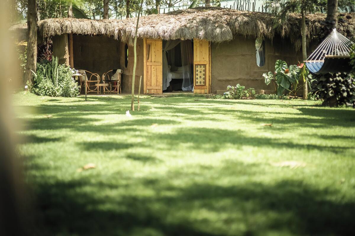 A thatched-roof hut with an open door, a hammock, and a small table with chairs in the foreground.