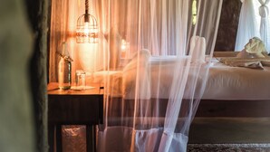 A room with a bed under a canopy, a bedside table with a lamp, and a patterned rug. - Mtoni river Lodge (Arusha)