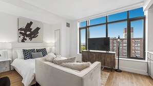 A modern bedroom with a large window, a bed, a sofa, a TV, and a desk.