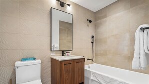 A modern bathroom with a toilet, wooden vanity, and a bathtub.