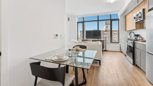 A modern kitchen with a large window, a dining area with a glass table, and a sofa.