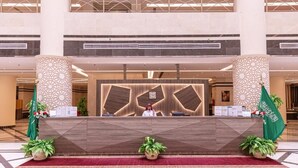 Zona de recepción de hotel con diseño moderno, que incluye un mostrador central, dos pilares decorativos y una alfombra roja.