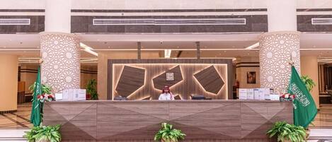 A hotel reception area with a modern design, featuring a central desk, two decorative pillars, and a red carpet.