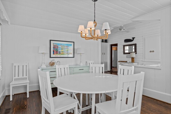 A white dining room with a round table and chairs, a chandelier, and a framed picture on the wall.