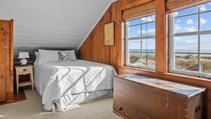 Een slaapkamer met een groot bed, een nachtkastje, een dressoir en een raam met uitzicht op het strand.