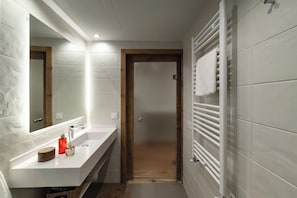 A modern bathroom with a white vanity, a mirror, a towel rack, and a shower area. - La Casa del Orfebre (Cuenca)