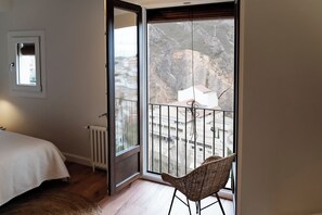 A bedroom with a large window, a radiator, a bed, and a wicker chair. - La Casa del Orfebre (Cuenca)