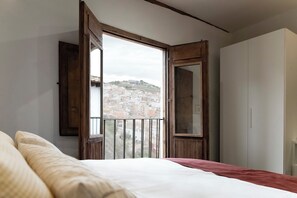 A bedroom with a bed, a wardrobe, and a balcony with a view of a town.