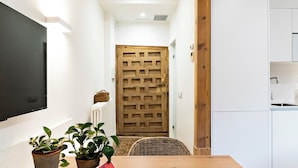 A narrow hallway with a wooden door, a wicker chair, and a table with books and a plant. - La Casa del Orfebre (Cuenca)