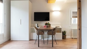 A modern kitchen with a dining table, two wicker chairs, a flat-screen TV mounted above the table, and a potted plant. - La Casa del Orfebre (Cuenca)