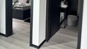 A modern bedroom with a bed, bedside table, and a wardrobe. There is a hallway leading to another room.