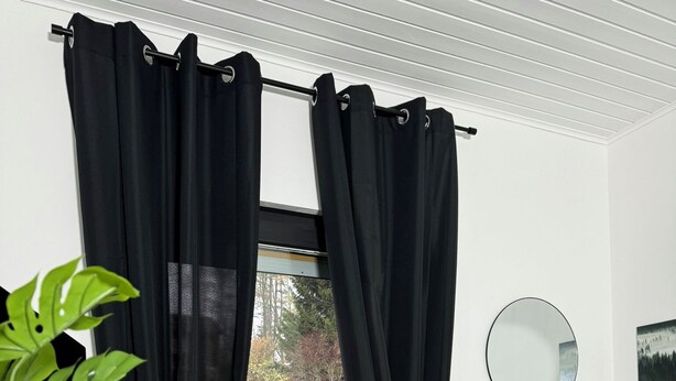 A bedroom with a bed, a window with black curtains, a potted plant, a radiator, and a wall-mounted mirror.