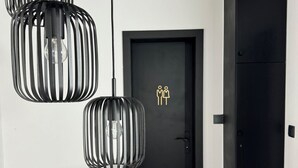 A modern hallway with three black pendant lights, a black door with a gold icon, and a staircase with a black railing.