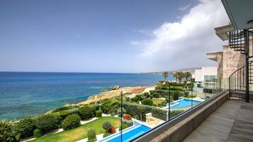 A balcony with a view of the sea, a swimming pool, and a landscaped garden.