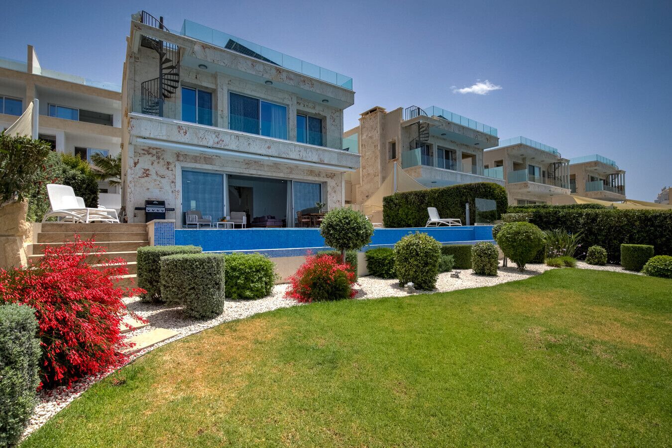 A modern multi-story building with a swimming pool, well-maintained garden, and outdoor seating area.