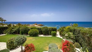 Paisaje costero con vista despejada al mar, un jardín cuidado con arbustos variados y un camino que lleva a una puerta.