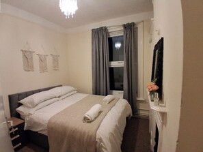 A neatly made bed with a rolled towel, a bedside table, and a window with curtains. - Sunset View Apartment in Southampton (Southampton)