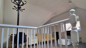 Une pièce avec une rambarde blanche, un porte-manteau noir, un canapé jaune et une armoire blanche.
