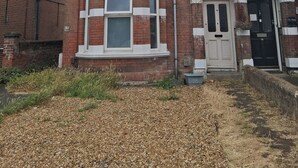 Une maison à deux étages, construite en briques, avec une baie vitrée, une porte d’entrée dotée d’un petit porche et le chiffre « 9 » bien visible sur le mur.