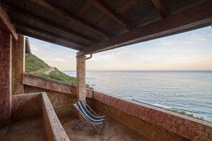 A covered outdoor area with a view of the sea, a stone bench, and a striped lounge chair. - Villa Seaside Sardegna (Villaputzu)