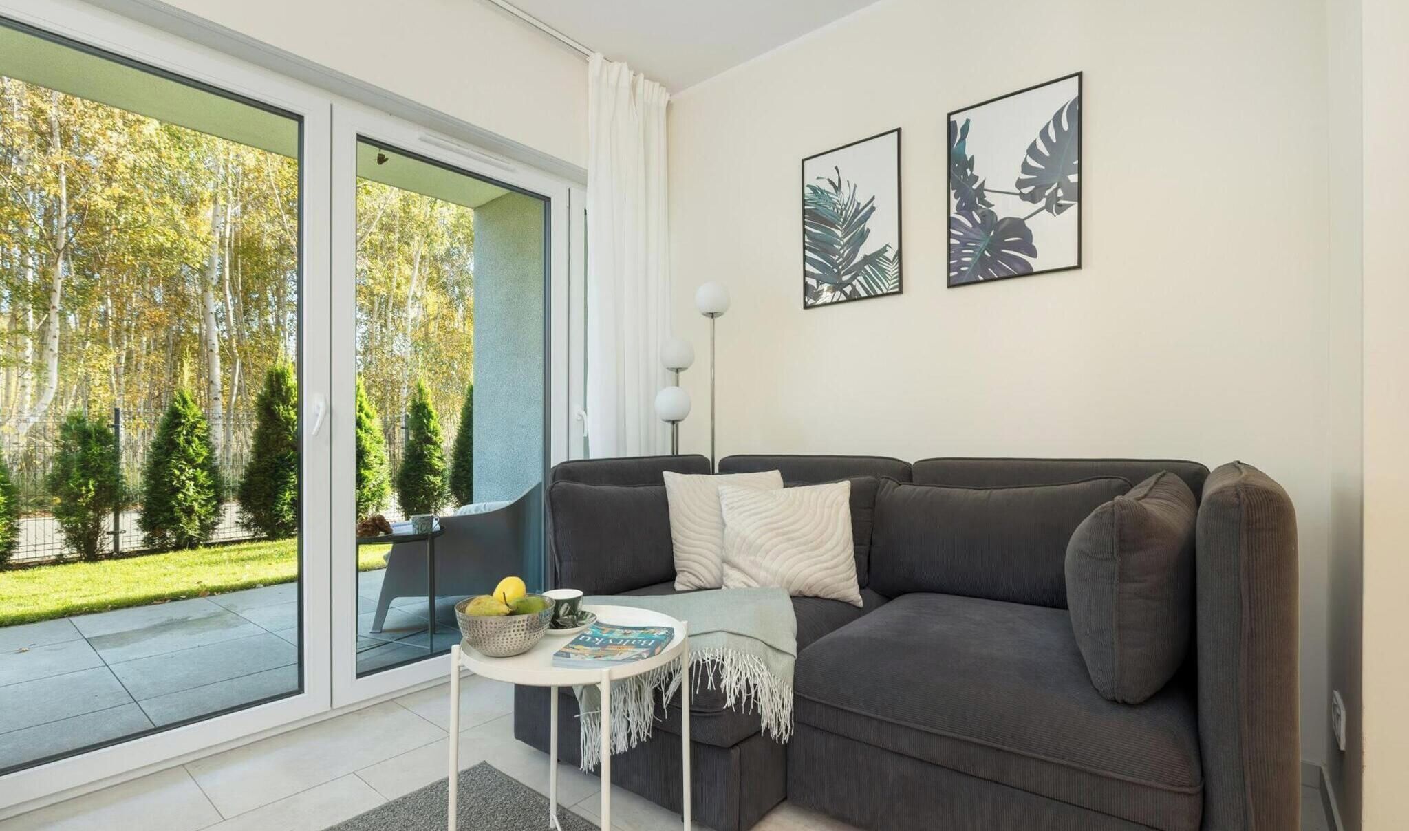 Un salon moderne avec un canapé gris, une petite table ronde sur laquelle repose un magazine, et une grande porte-fenêtre coulissante donnant sur un jardin.