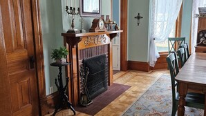 Ett traditionellt matrum med ett träbord, stolar, en öppen spis och en mönstrad matta.