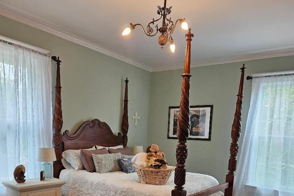 A bedroom with a four-poster bed, a chandelier, a floral rug, and a nightstand.