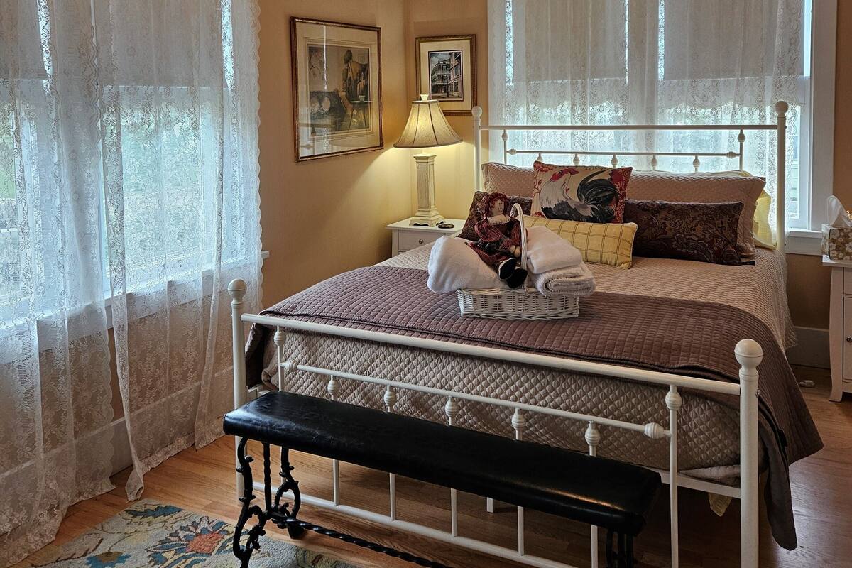 A bedroom with a bed, a bench, a nightstand, a lamp, and two framed pictures on the wall.