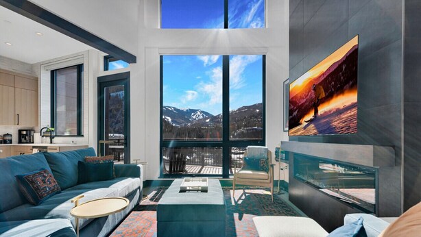 A modern living room with a large window offering a mountain view, a cozy seating area, and a flat-screen TV mounted on the wall.